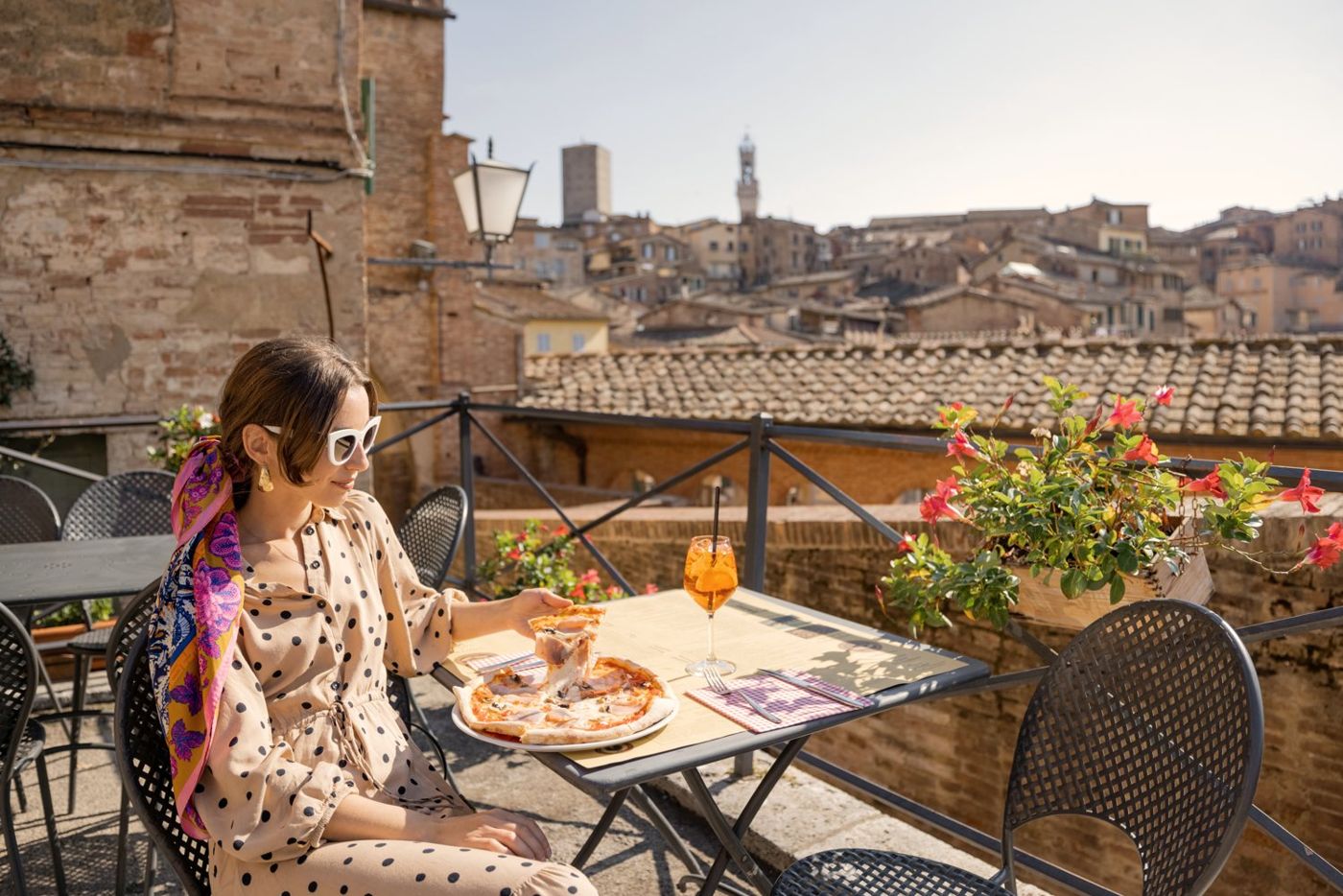 A traveler has lunch on a terrace above the rooftops of Siena.